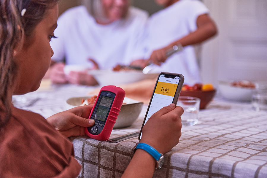 Flicka kollar på insulinpump och telefon med blodsockerkurva