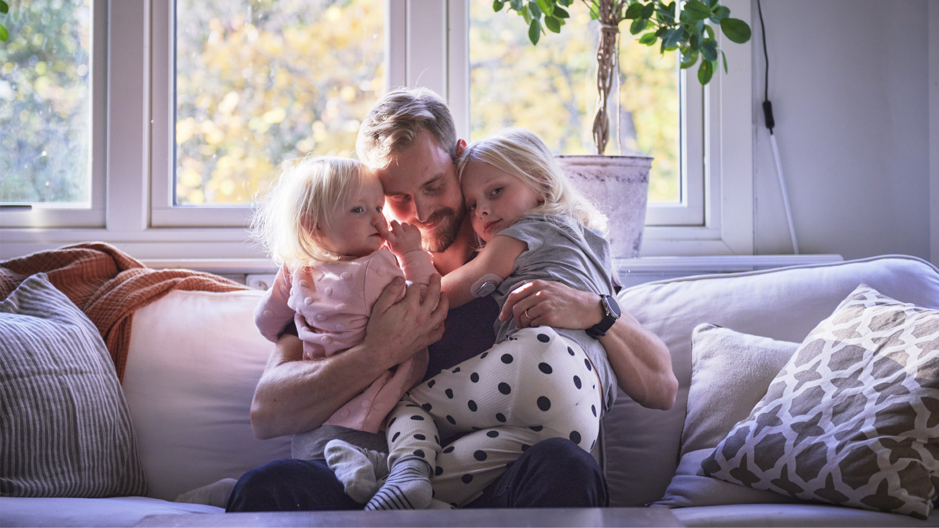 Pappa kramar två döttrar i soffan, en av dem har typ 1-diabetes