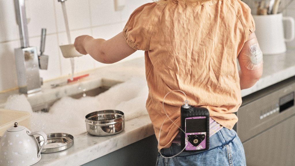 Barn med insulinpump står och leker i diskhon